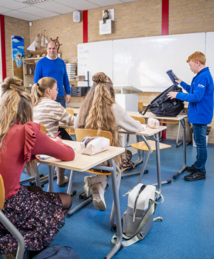 Leerlingen en docent in een klaslokaal van locatie Tholen, klas wacht op leerling die een boek uit zijn tas pakt