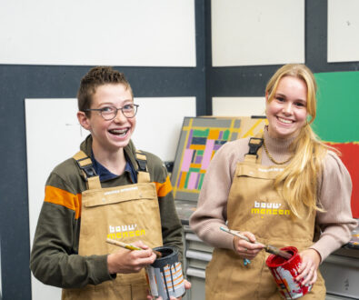 Leerlingen van de afdeling bouwen, wonen en interieur staan met een verfpot in de hand en lachen in de camera