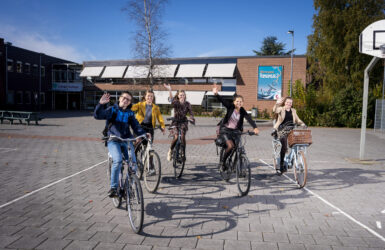 Leerlingen fietsen van het plein af en zwaaien in de camera