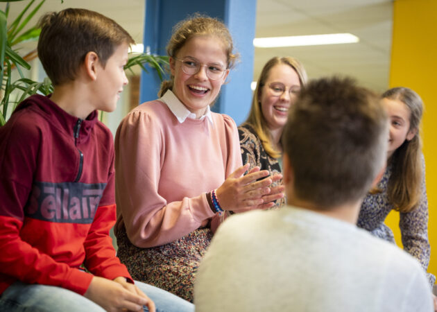 Leerlingen klapt enthousiast in de handen in gesprek met andere leerlingen.