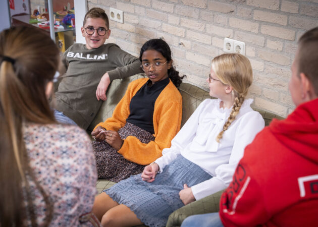 Leerlingen zitten op een bank in de aula en kletsen met elkaar.