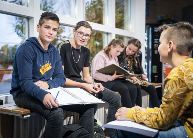 Leerlingen van locatie Goes Noordhoeklaan zitten in de gang samen huiswerk te maken.