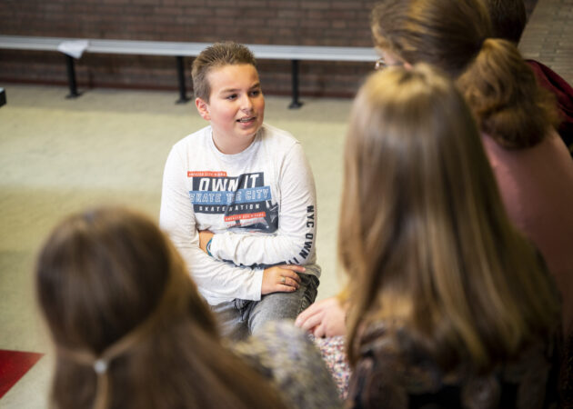 Leerling praat met leerlingen in de aula.