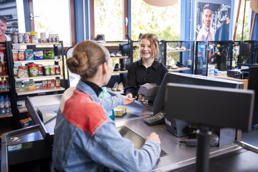 Een leerling achter de kassa helpt een andere leerling op de afdeling economie en ondernemen van locatie Krabbendijke Kerkpolder