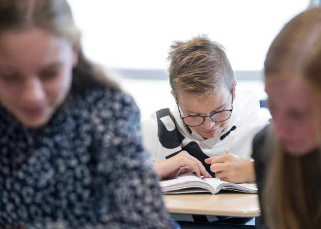 Leerling leest in boek in de klas op het Calvijn College.