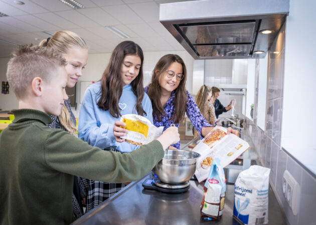 Leerlingen en docent in het verzorgingslokaal, ze krijgen uitleg over hoe ze het recept moeten bereiden