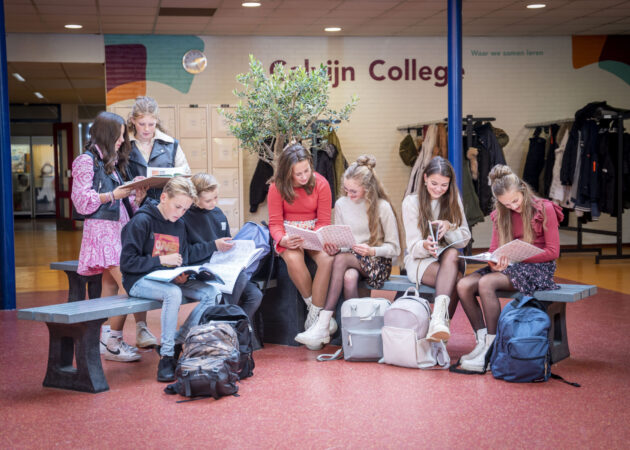Groep leerlingen in de gang van het Calvijn College, samen leren uit een boek.