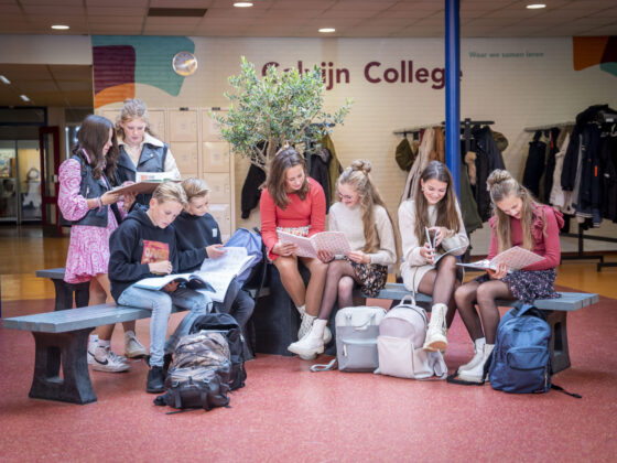 Leerlingen in de gang van locatie Tholen, zittend op een bankje met een boek. Samen leren!