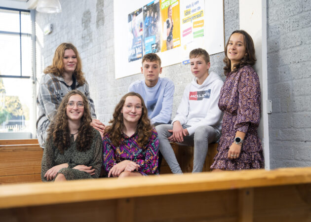 Leerlingen zitten op bankje en lachen naar de camera in de aula van locatie Krabbendijke Kerkpolder